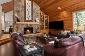 Ein modernes Wohnzimmer mit Kamin aus Stein, Ledersofas, einem Bücherregal und einem großen Fernseher.