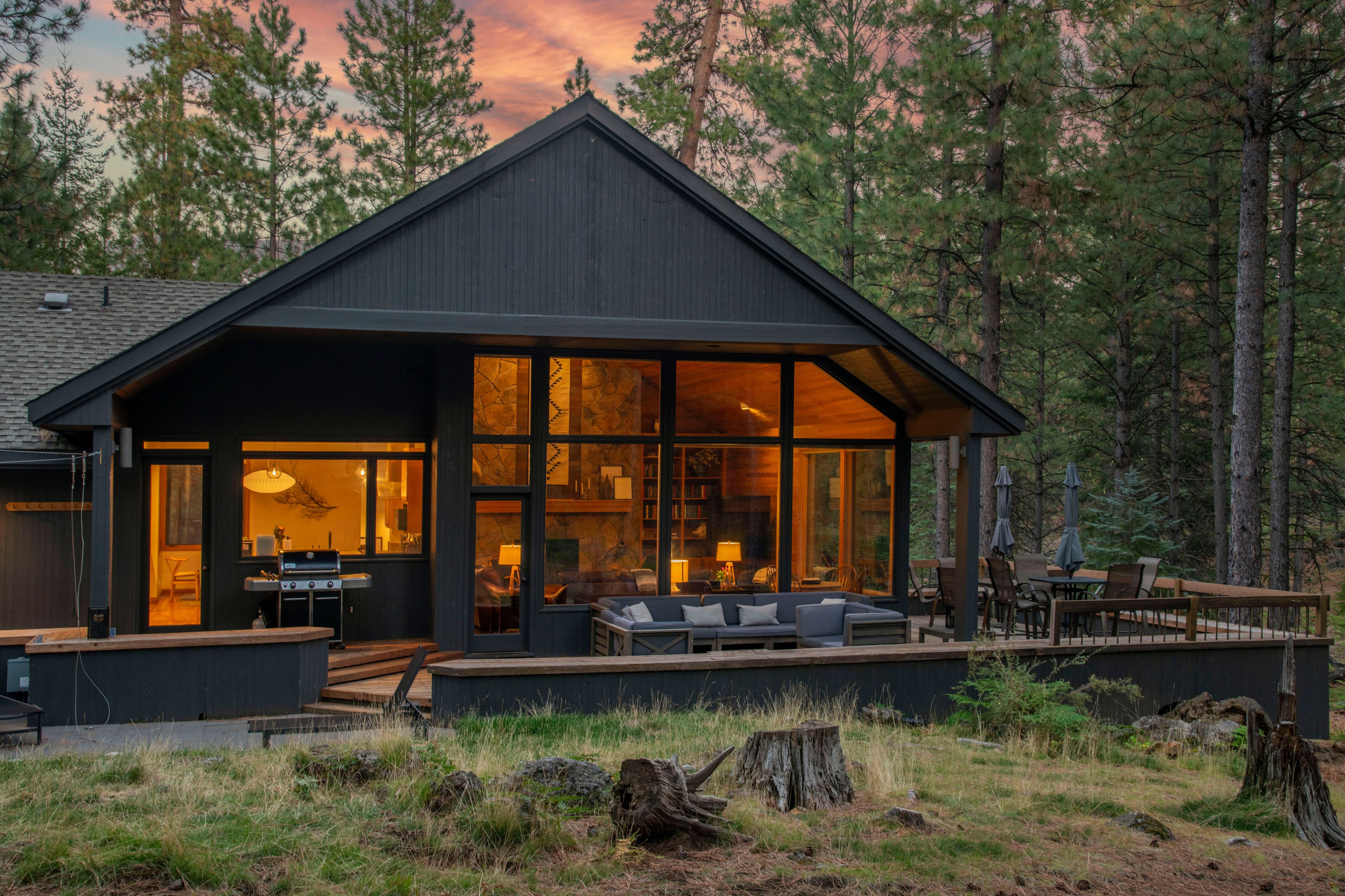 Exterior dusk view of the cabin and deck surrounded by pine trees.