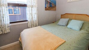 Une chambre à coucher avec un lit, une fenêtre avec des rideaux, un tableau au mur et une tête de lit en rotin.