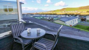 Un balcon avec une table et des chaises, donnant sur un terrain de camping où se trouvent de nombreuses caravanes et des maisons.