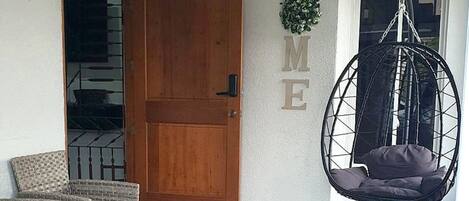 A room with wicker furniture, a hanging chair, and a wooden door.