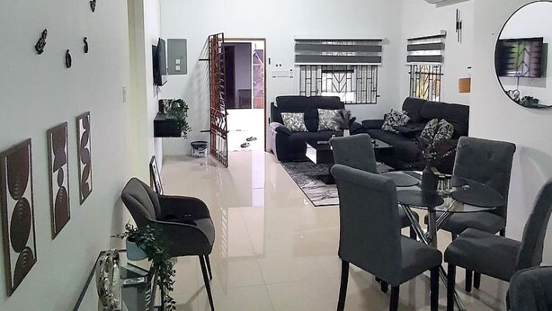 A spacious living area with a high ceiling, a ceiling fan, a sofa set, a dining table with chairs, and a TV mounted on the wall. - DraxHall Villa (Saint Ann's Bay)