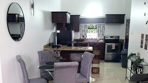 A modern kitchen with dark cabinets, a central island, and a dining area with grey chairs. - DraxHall Villa (Saint Ann's Bay)