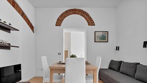 A modern living room with a dining area, white walls, a brick archway, a flat-screen TV, and a grey sofa. - BLI39 Cozy apartment in the Bocconi area (Milano)