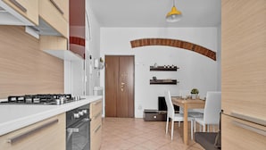 A modern kitchen with a gas stove, oven, and white cabinetry. There is a dining area with a table and chairs, and a brick archway on the wall. - BLI39 Cozy apartment in the Bocconi area (Milano)