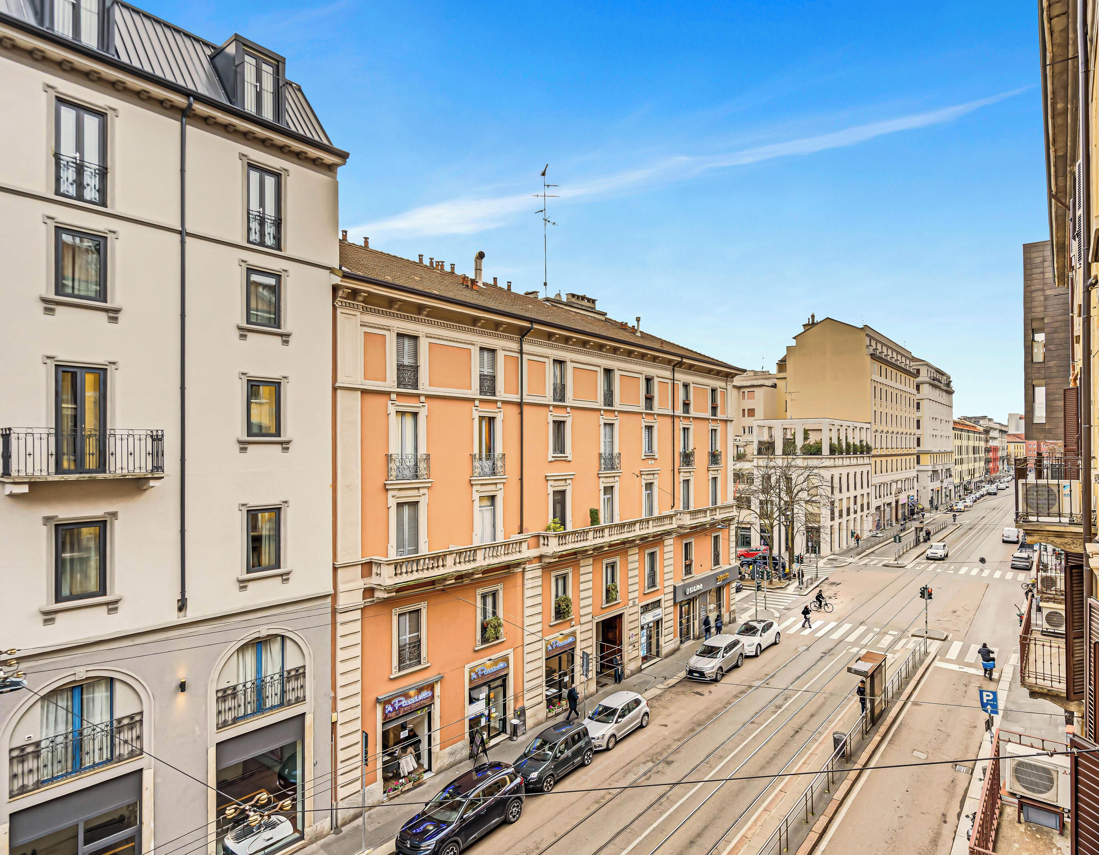 Une vue de rue d’une ville avec des immeubles à plusieurs étages, une ligne de tramway et des voitures garées.