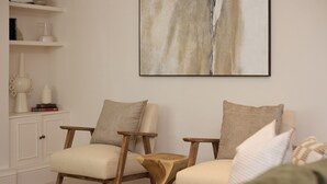 Un salon avec deux fauteuils en bois, une petite table en bois et un grand tableau abstrait accroché au mur.