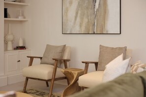 Ein Wohnzimmer mit zwei Holzstühlen, einem kleinen Holztisch und einem großen abstrakten Gemälde an der Wand.