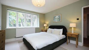 Une chambre à coucher avec un lit, deux tables de chevet avec des lampes, un radiateur, une fenêtre avec des stores et un tableau au mur.