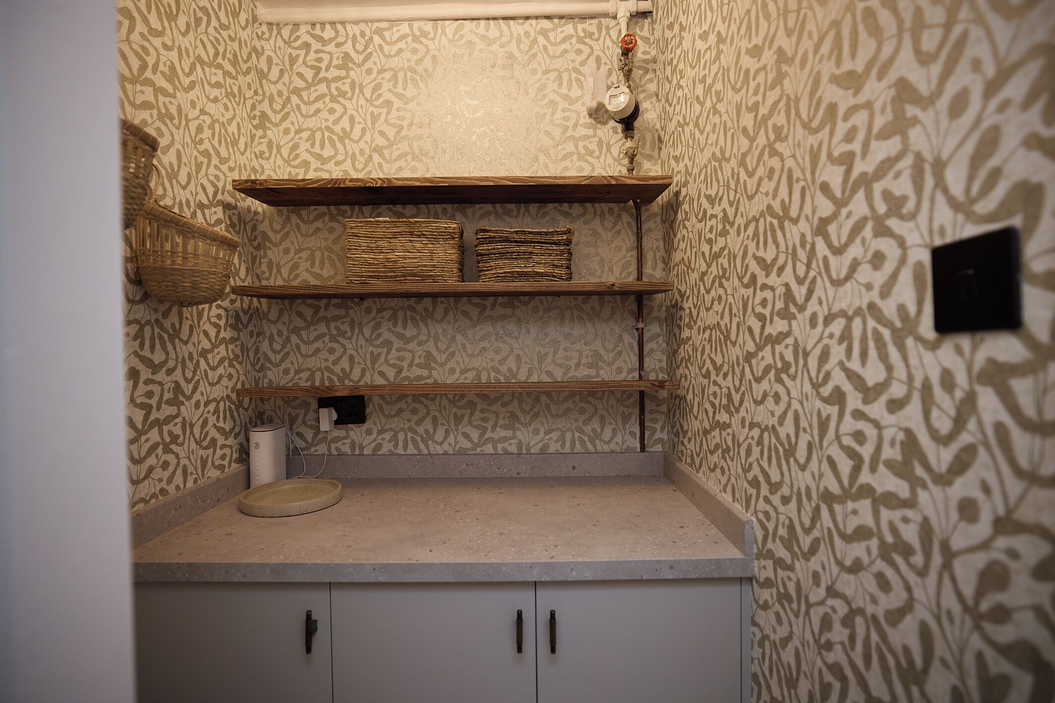 A bathroom with patterned wallpaper, a shelf with baskets, a toilet paper holder, and a sink.