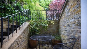 Un mur de briques avec un escalier en métal, une table ronde en métal et deux chaises en métal dans une cour.