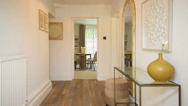 Un couloir doté d’un plancher en bois, d’une console en verre sur laquelle est posé un vase, d’un grand miroir et d’œuvres d’art encadrées accrochées aux murs.