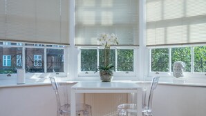 Un coin repas avec une table et des chaises blanches, un vase rempli de fleurs et une statue posée sur le rebord de la fenêtre.