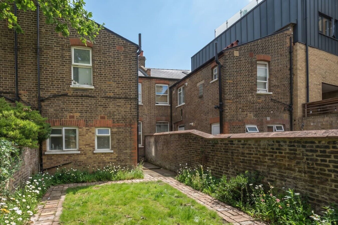 A courtyard with brick buildings, a brick wall, and a grassy area with flowers.