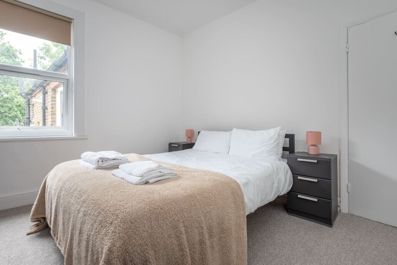 A bedroom with a bed, a window, a nightstand, and a door.