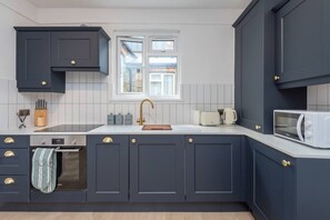 A modern kitchen with dark cabinetry, a white countertop, a built-in oven, a microwave, and a window above the sink. - Kilburn Flat w/ Designer Kitchen near Kensal Rise (Greater London)