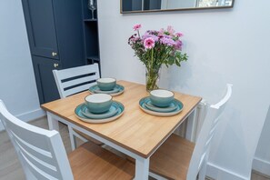 A dining table with four bowls and saucers, a vase with flowers, and white chairs. - Kilburn Flat w/ Designer Kitchen near Kensal Rise (Greater London)
