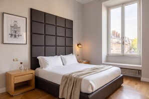 A bedroom with a large bed, a headboard, a bedside table, a nightstand, a framed picture, a window with a view, and a radiator. - Sant'Angelo Deluxe Apartment (Roma)