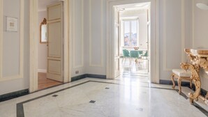 En rymlig hall med marmorgolv, utsmyckade guldfärgade möbler och en kristallkrona.