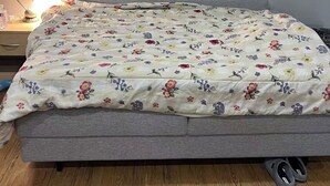 Quarto com uma cama, uma mesinha de cabeceira, abajur, um par de chinelos e um quadro na parede.