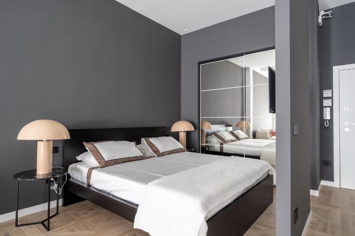A modern bedroom with a large bed, two bedside tables, and a mirror.
