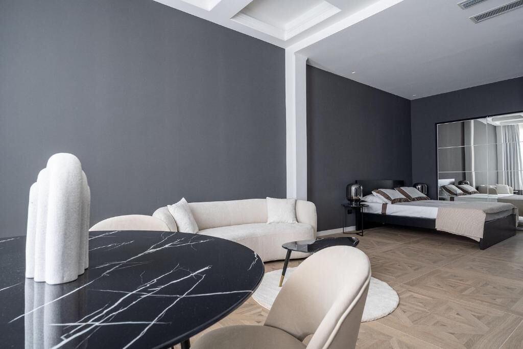 A modern hotel room with a bed, a sofa, a dining table, and a large mirror.