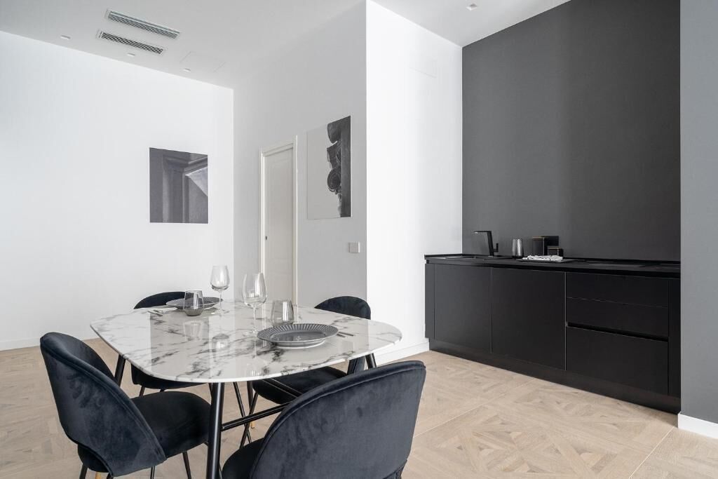 A modern kitchen with dark cabinets, a marble countertop, and a dining area with a marble table and black chairs.