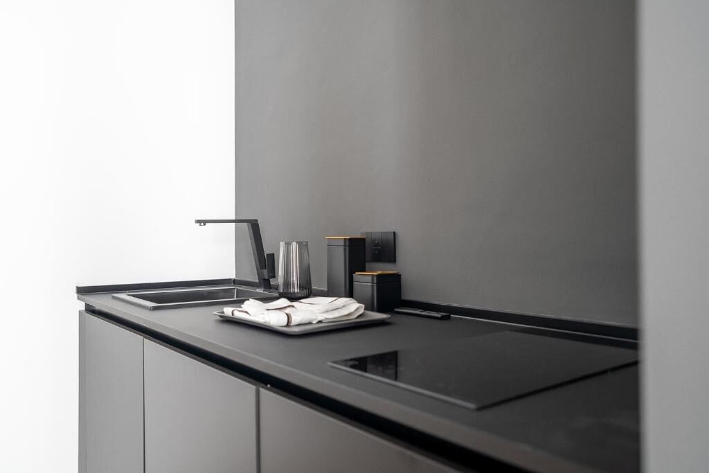 Una cocina moderna con encimera negra, pileta de acero inoxidable y un florero de vidrio.