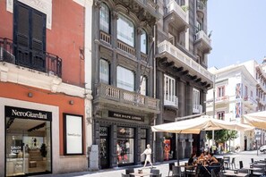 A street with outdoor seating, storefronts including NereoGiardini and Polo Ralph Lauren, and a building with balconies.