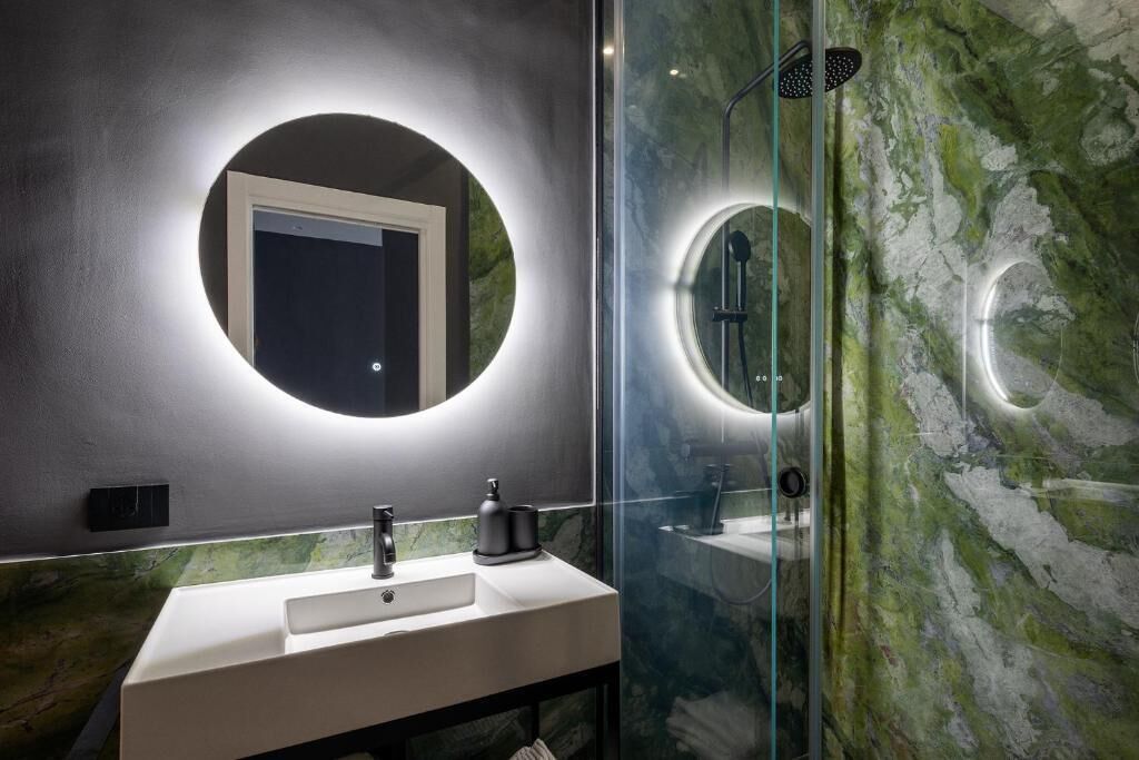 A modern bathroom with a round mirror, a white sink, and a glass shower enclosure.