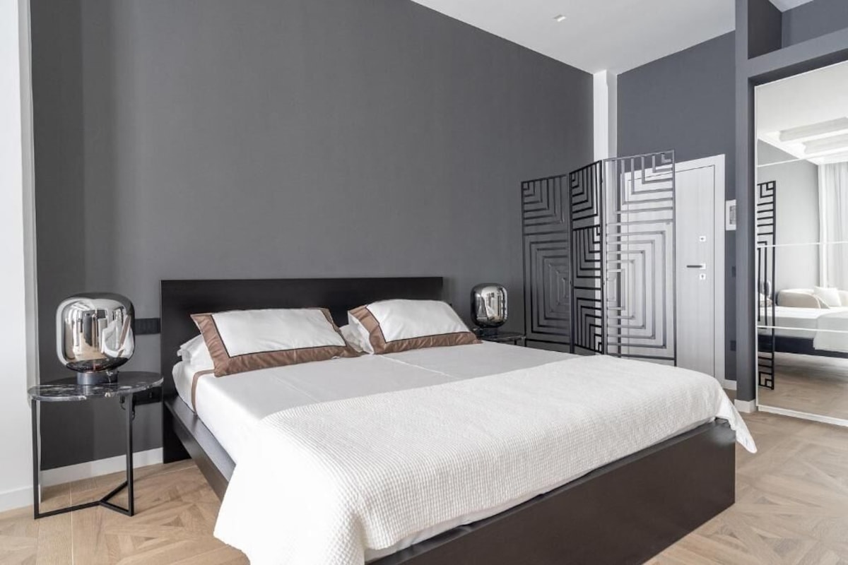 A modern bedroom with a large bed, a nightstand, a mirror, and a wardrobe with geometric patterns.
