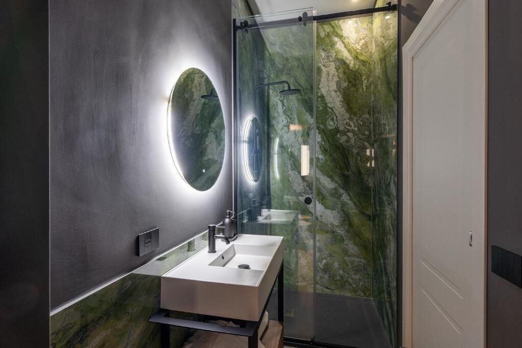 Un baño moderno con ducha de vidrio, un espejo grande y un lavabo blanco.