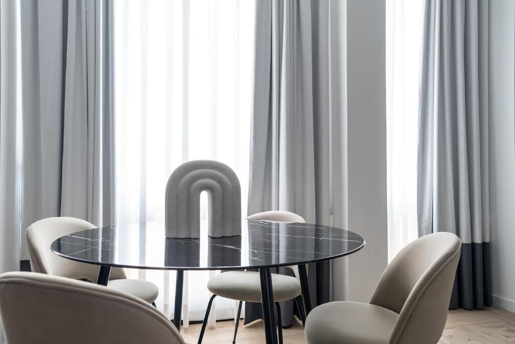 A modern dining area with a round glass table, four chairs, and a unique curved backrest chair.