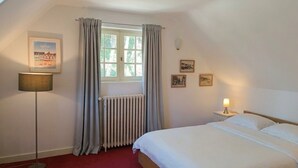 Une chambre à coucher avec un lit, un radiateur, une fenêtre avec des rideaux, une lampe sur pied et des tableaux encadrés accrochés au mur.