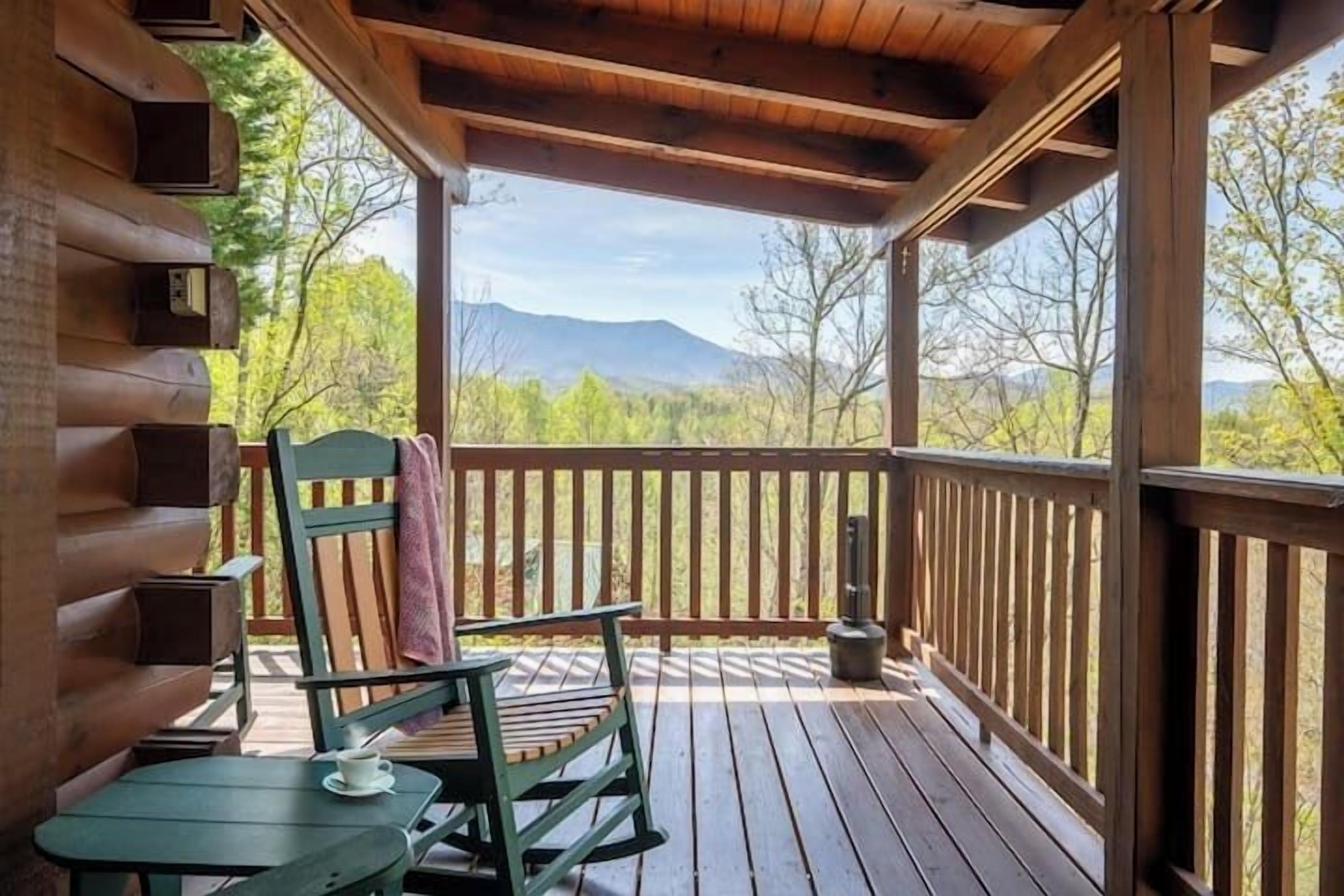 A wooden deck with a view of mountains, a chair, a table, and a hanging lantern.