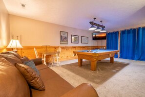 Une pièce confortable avec une table de billard, un canapé et un téléviseur.