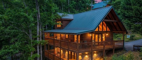 A log cabin with a balcony, surrounded by dense forest.