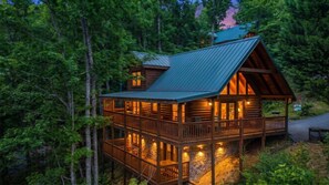 A log cabin with a balcony, surrounded by dense forest. - Bear Ridge | Luxury 3BR Smoky Mountain Cabin | Hot Tub, Game Room & Pool Access (Gatlinburg)