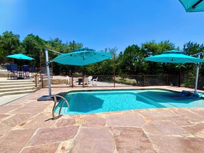 Una piscina amb rajoles de pedra, dues ombrel·les i una zona de seients amb cadires.