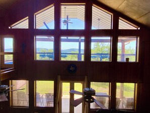 Ein mehrgeschossiges Zimmer mit großen Fenstern, einem Deckenventilator und Blick auf Gartenmöbel.