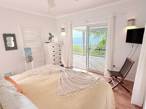 Une chambre à coucher comprenant un lit, une chaise, une commode, un téléviseur et un balcon avec vue sur l’océan.