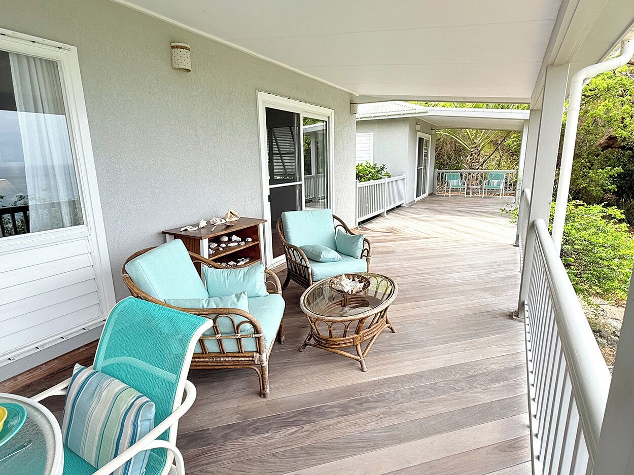 A covered porch with wicker furniture, a wooden floor, and a view of the surrounding greenery.