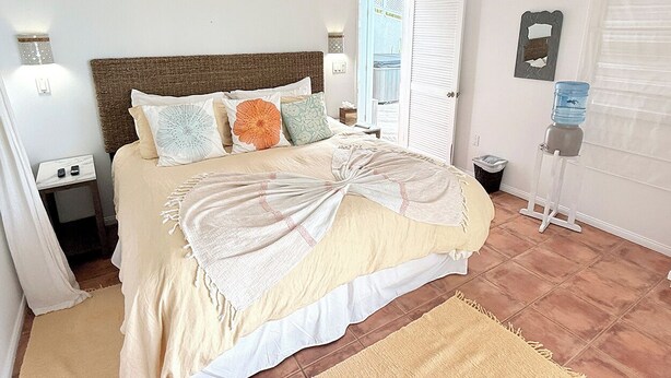 Un dormitorio con cama, mesitas de noche, dispensador de agua y ventana con persianas.