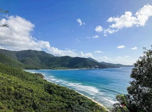 Un paysage côtier avec un ciel dégagé, une plage et des collines boisées.