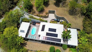 Vista aérea de una casa moderna con piscina, paneles solares y un jardín ajardinado.