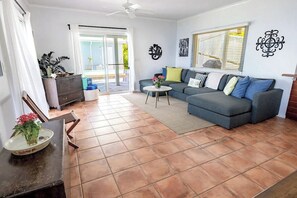 A living room with a grey sofa, a coffee table, and a dining area with a table and chairs. - Brizan Villa – Private 3 Bedroom Caribbean Retreat with Pool, Hot Tub & Stunning Reef Bay Views in St. John, USVI (St John)