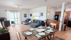 Un comedor con una mesa de madera preparada para seis personas, un sofá y una cocina al fondo.