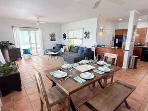 A dining area with a wooden table set for six, a sofa, and a kitchen in the background. - Brizan Villa – Private 3 Bedroom Caribbean Retreat with Pool, Hot Tub & Stunning Reef Bay Views in St. John, USVI (St John)
