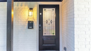 A black door with a glass panel and a metal gate, a mailbox, and a doormat with the text 'HOWDY HOWDY'. - Outdoor Cinema | Hot Tub | Fire Pit | Huge Yard (Houston)