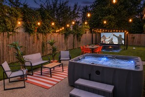An outdoor patio with a hot tub, seating area, and a TV screen displaying a movie. - Group Stay 4 Kanye | Reliant Stadium | Hot Tub | Cinema (Houston)